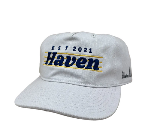 White cap with 'Haven' and 'Est 2021' text on a wooden surface