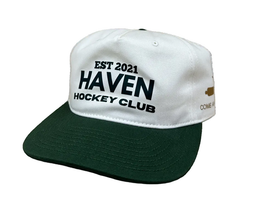 White and green cap with 'HAVEN HOCKEY CLUB' text on a wooden surface